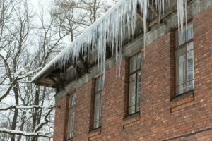 Ice stalactite hanging from the roof with red brick wall. Winter season.